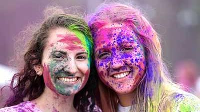 Two female students with their faces covered in color powerder from holi fest.